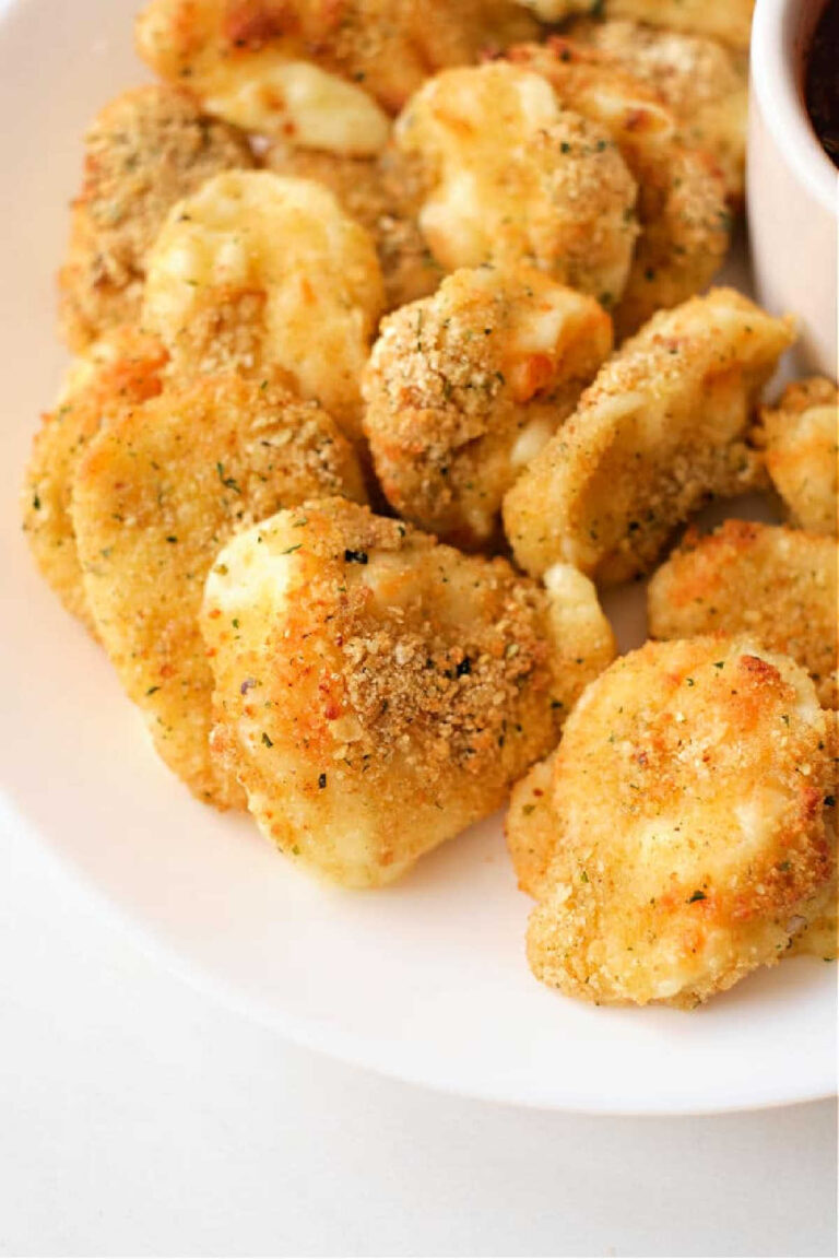 A plate of crispy, golden brown air fryer cheese curds, perfectly seasoned and mouth-wateringly delicious, with a small bowl of marinara sauce partially visible on the side.