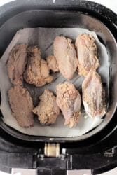 Firecracker chicken wings with seasoning sizzle in an air fryer basket lined with parchment paper.