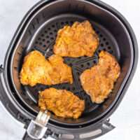 Four perfectly seasoned chicken thighs nestled in an air fryer basket, ready to transform into crispy fried delights.