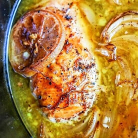 Close-up of crockpot lemon pepper chicken with caramelized onions simmering in a savory broth.