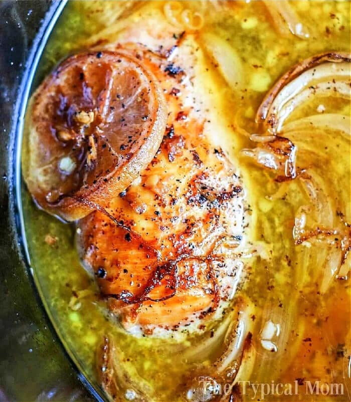 Close-up of crockpot lemon pepper chicken with caramelized onions simmering in a savory broth.