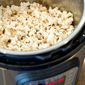 A metal pot brimming with freshly popped popcorn sits in an Instant Pot on the countertop. The control panel of the cooker is visible, showcasing a digital display.