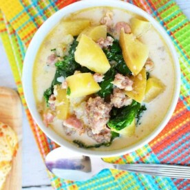 A bowl of creamy pressure cooker zuppa Toscana with potatoes, sausage, and kale rests on a colorful tablecloth beside a spoon.