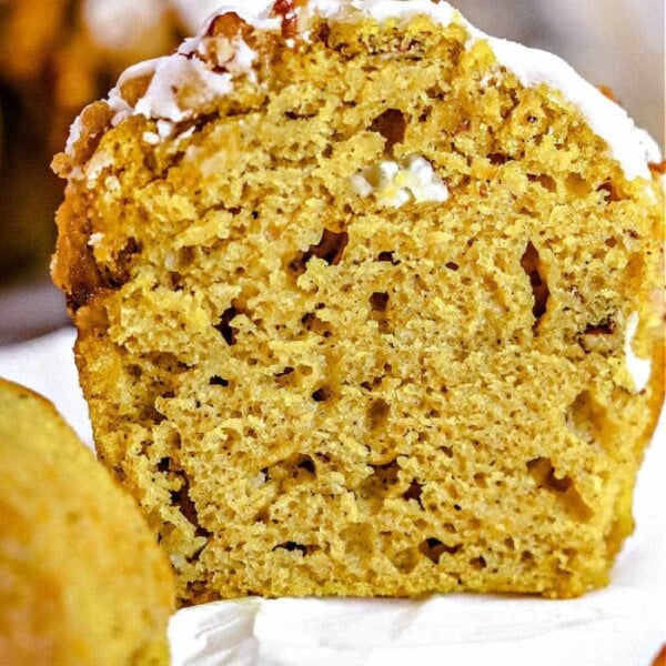 Close-up of a sliced mini pumpkin banana muffin topped with white icing, revealing a moist and fluffy texture.