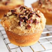 Close-up of a coffee cake muffin, boasting crumbly streusel and pecans, resting on a cooling rack.