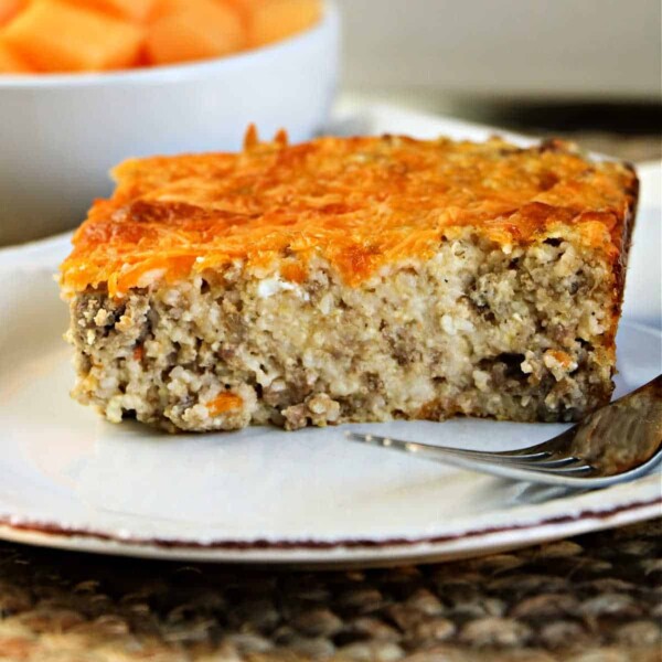 A slice of savory breakfast cheese grits casserole sits on a white plate with a fork beside it.