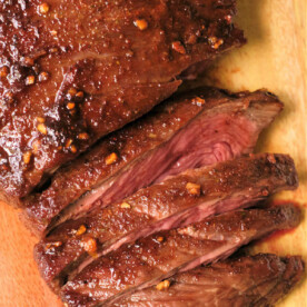 Sliced, juicy flank steak with a seared crust and garlic seasoning sits elegantly on a wooden cutting board, reminiscent of perfectly cooked air fryer flank steak.