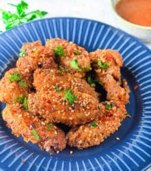 Crispy firecracker air fryer chicken wings garnished with sesame seeds and parsley on a blue plate.