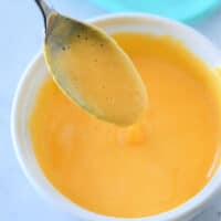 A spoon dipped in a bowl of creamy orange cheese sauce showcases the perfect velveeta blend, demonstrating how to make velveeta cheese sauce effortlessly delicious.