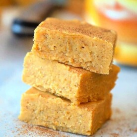 Three stacked microwave pumpkin fudge squares on parchment paper, sprinkled with cinnamon.