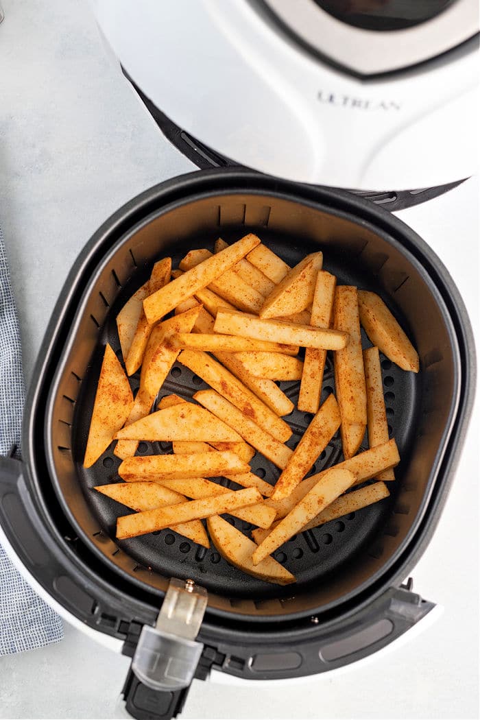 The image shows a black air fryer basket filled with seasoned, cut potato fries. The air fryer is open, revealing the fries inside. The appliance brand "Ultrean" is visible on the open lid. On a light-colored surface, these delicious fries could easily be swapped for turnip fries to enjoy a unique twist.