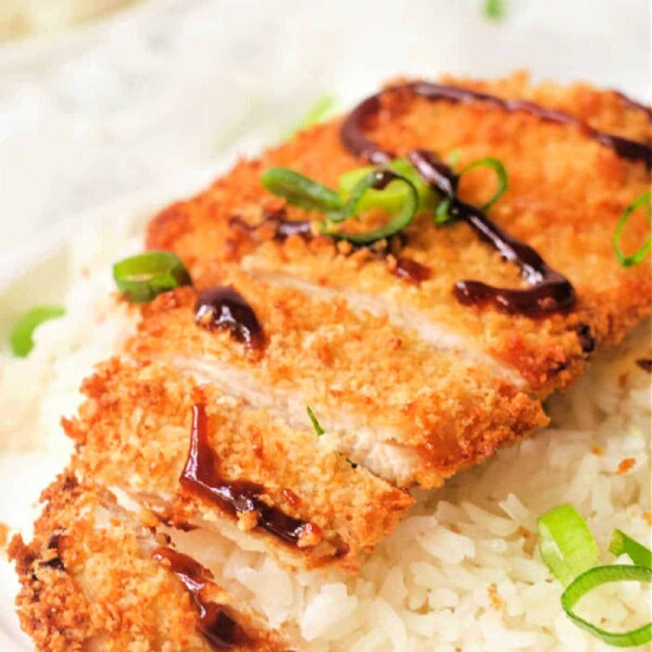 A plate with white rice topped with sliced, air fryer chicken katsu drizzled with dark sauce and garnished with sliced green onions.