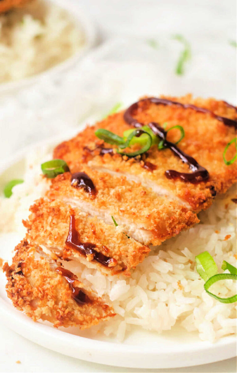 A plate with white rice topped with sliced, air fryer chicken katsu drizzled with dark sauce and garnished with sliced green onions.