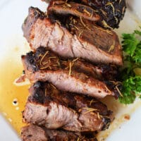 Air fryer chuck roast sliced and grilled, garnished with rosemary on a white plate, accompanied by a sprig of parsley.