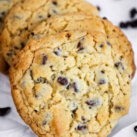 Four Bisquick chocolate chip cookies rest on a white surface, surrounded by scattered chocolate chips.