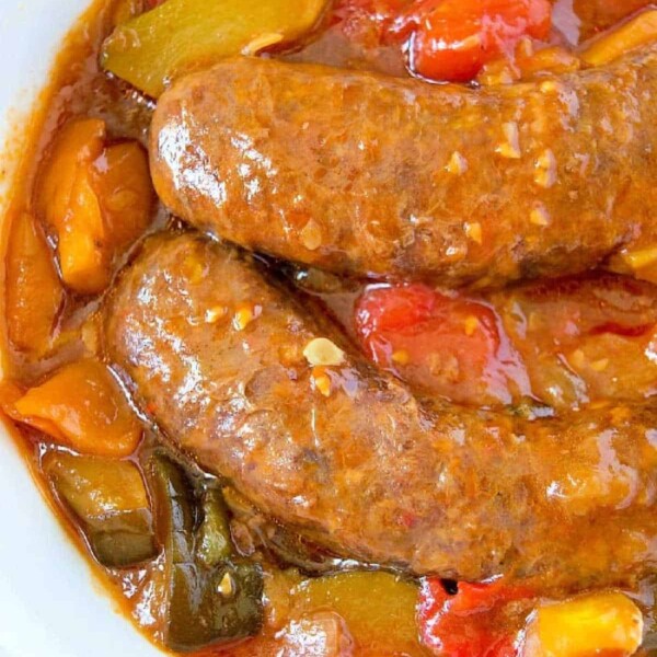 Crockpot sausage simmered in a tomato-based sauce with vibrant red and yellow bell peppers, served in a white bowl.