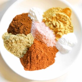 A white plate with piles of vibrant spice powders, including gingerbread spice ingredients, and coarse salt, arranged artfully.