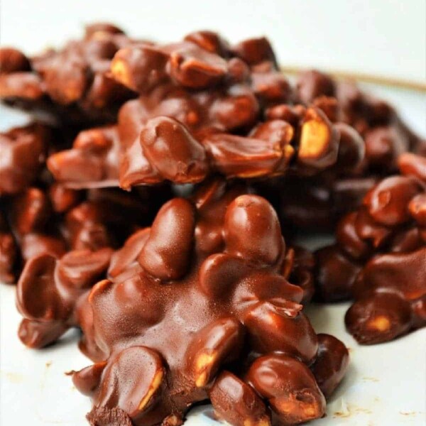 A delightful mound of crockpot chocolate candy sits on a white surface, revealing clusters of nuts beneath the smooth coating.