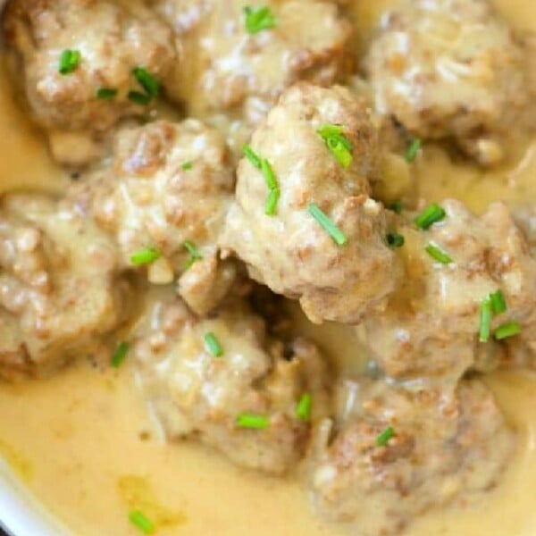 Creamy meatballs garnished with fresh chives in a white bowl, featuring a rich Swedish meatball sauce with sour cream.