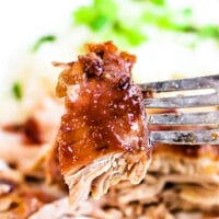 Close-up of a fork holding a bite of succulent pulled pork with sauce, garnished with herbs, evoking the rich flavors reminiscent of slow cooker BBQ chicken thighs.