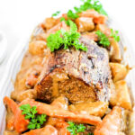 A plate of tender sirloin tip roast, slow-cooked to perfection with carrots, potatoes, and a parsley garnish, all generously covered in savory gravy.