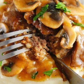 Close-up of Instant Pot Salisbury steak with mushroom gravy and mashed potatoes, garnished with parsley, being cut with a fork.