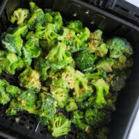 Frozen broccoli, perfectly seasoned, waits in the tray of an air fryer, ready to be cooked to crispy perfection.