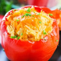 A red bell pepper bursting with savory rice and tender chicken, topped with melted cheese and a sprinkle of parsley.