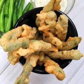 A bowl of perfectly crispy fried green beans served with a flavorful dipping sauce and a side of fresh green beans.