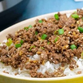 A bowl of fluffy white rice topped with Instant Pot Korean beef and a sprinkle of chopped green onions.