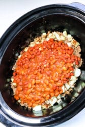 Close-up of a crockpot with venison chili, featuring baked beans, onions, and ground beef.