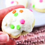 A hand holds a frosted Italian Easter cookie adorned with vibrant, flower-shaped sprinkles.