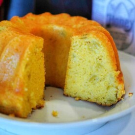 A close-up of a sliced bundt cake on a white plate reveals its golden-brown exterior and light, fluffy interior, reminiscent of air fryer cornbread. A bottle with a honey label is partially visible in the background.