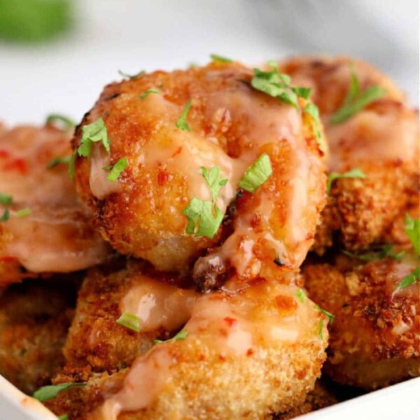 Close-up of crispy fried shrimp, reminiscent of air fryer bang bang shrimp, topped with a creamy sauce and garnished with fresh herbs in a white dish.