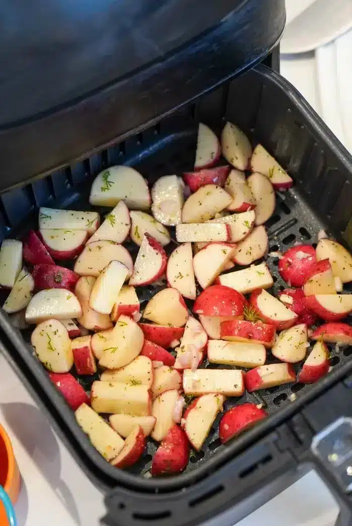 Chopped air fryer red potatoes seasoned with herbs are placed in the basket, ready for cooking.