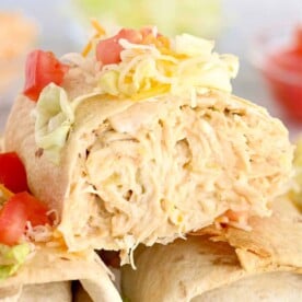 Close-up of air fryer chimichangas filled with shredded chicken, topped with cheese, lettuce, and diced tomatoes.