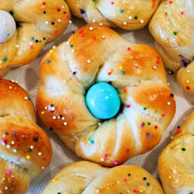 Close-up of baked brioche rolls with sprinkles, each resembling a festive Easter egg bread, topped with a blue candy egg at the center.