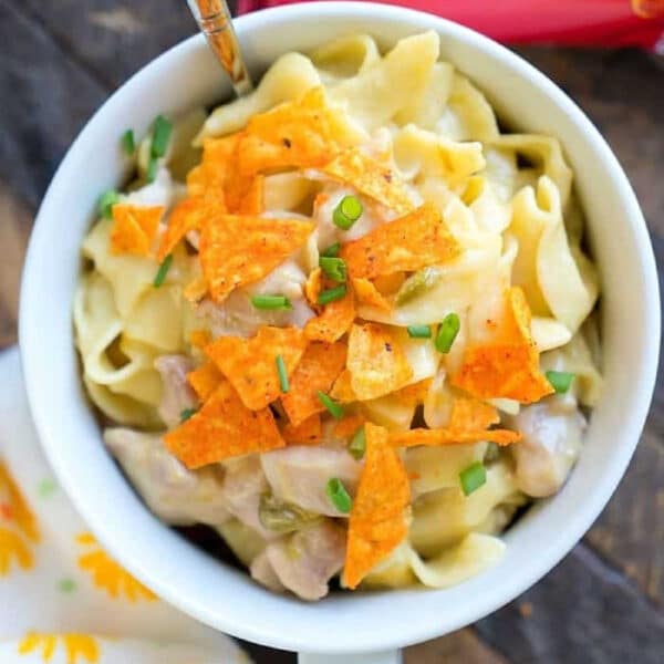 A bowl of creamy pasta reminiscent of a pressure cooker Dorito casserole, topped with crushed Doritos and chopped chives, sits beside a spoon and a Doritos bag.