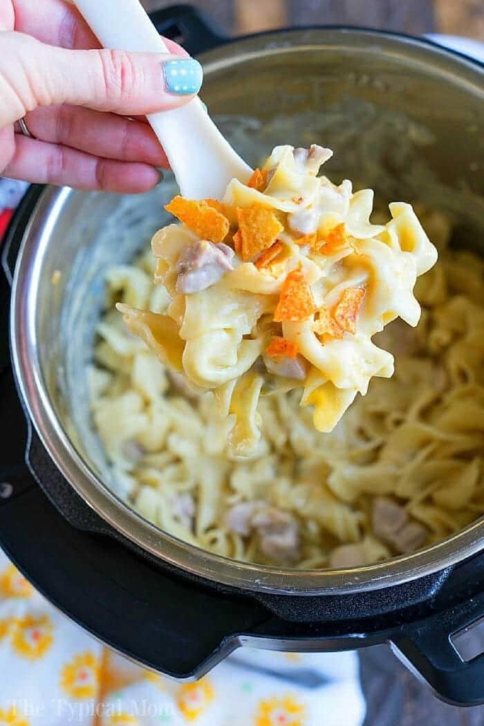 A hand holds a spoonful of creamy noodle casserole with chicken and carrots over an Instant Pot, perfect for recreating your favorite pressure cooker Dorito casserole.