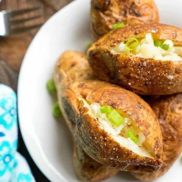 Baked potatoes on a white plate, topped with butter and chopped green onions, add a delightful touch to any meal. For those who prefer smoking their potatoes, understanding how long to smoke potatoes at 250 can enhance the flavor and texture beautifully.