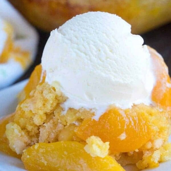 A plate of dump peach cobbler topped with a scoop of vanilla ice cream.