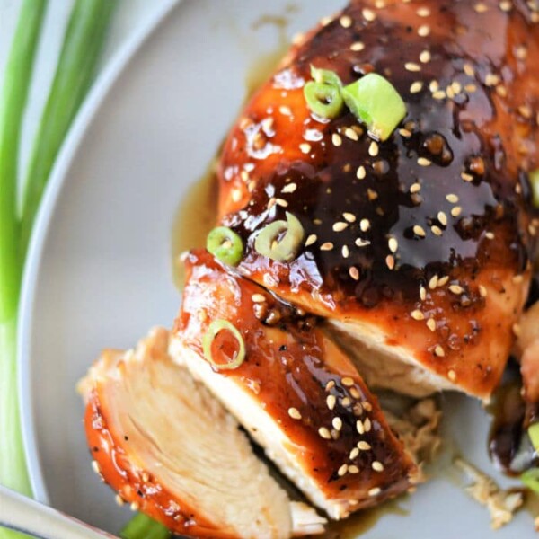 Sliced teriyaki chicken breast on a plate, topped with sesame seeds and green onions, crafted from a simple teriyaki chicken recipe using bottled sauce, with a fork beside it.