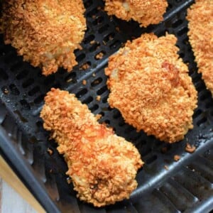 Golden-brown, crispy-fried gluten-free chicken wings inside an air fryer basket, resting on a wooden surface.