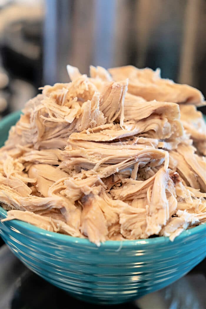 Tender shredded cooked chicken piled high in a blue bowl—see How to Make Shredded Chicken on the Stove for this easy and delicious result.