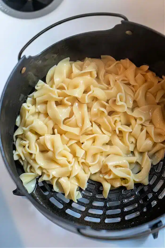 Cooked pasta noodles glisten in a black colander, showcasing their glossy texture from above. Their silky appearance suggests they've been transformed into delicious Ninja Foodi butter noodles, capturing the essence of creamy perfection as they rest in the strainer.