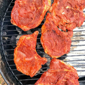 Five seasoned pork chops, perfectly prepared with a flavorful dry rub, are lined up on the grill, ready for cooking.