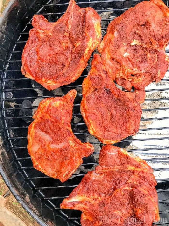 Five seasoned pork chops, perfectly prepared with a flavorful dry rub, are lined up on the grill, ready for cooking.