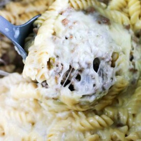 Close-up of creamy, cheesy rotini pasta with ground meat, reminiscent of a savory instant pot cheesesteak dish, being scooped with a serving spoon.