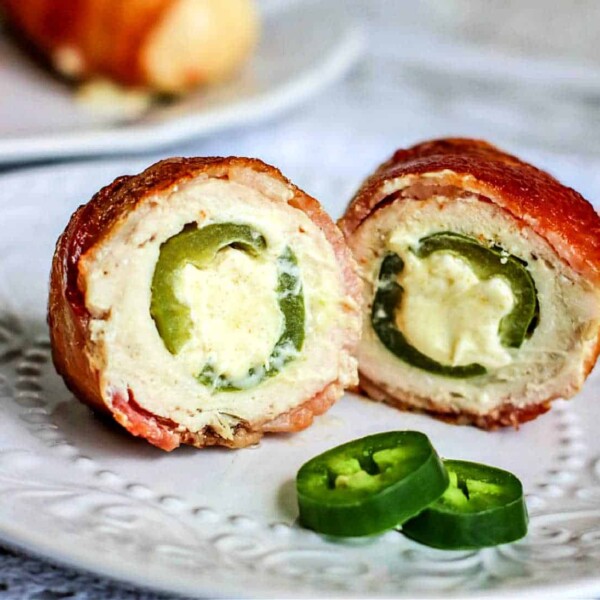 A close-up of an air fryer stuffed chicken breast wrapped in crispy bacon and filled with jalapeño and cream cheese. The dish is elegantly presented on a decorative white plate, accompanied by a few fresh jalapeño slices for an extra kick.