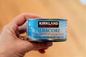 A hand holds a can of Kirkland Signature Albacore Solid White Tuna in Water, perfect for pairing with crockpot chicken dishes made from frozen breasts.